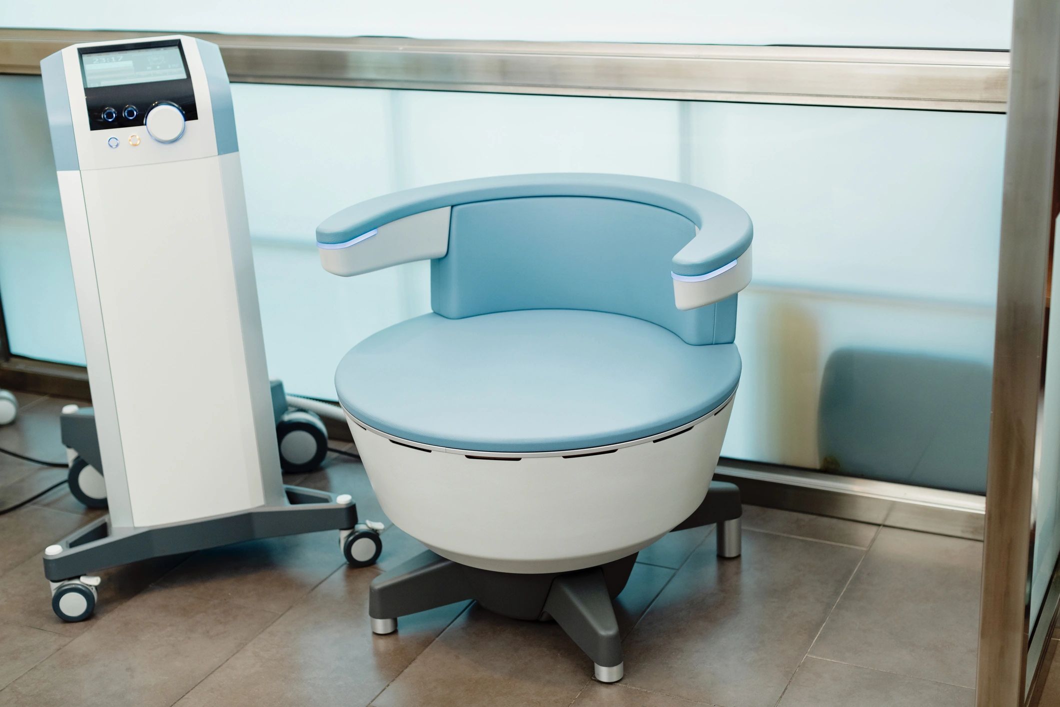 A modern, round medical device with a padded seat and control panel on wheels.
