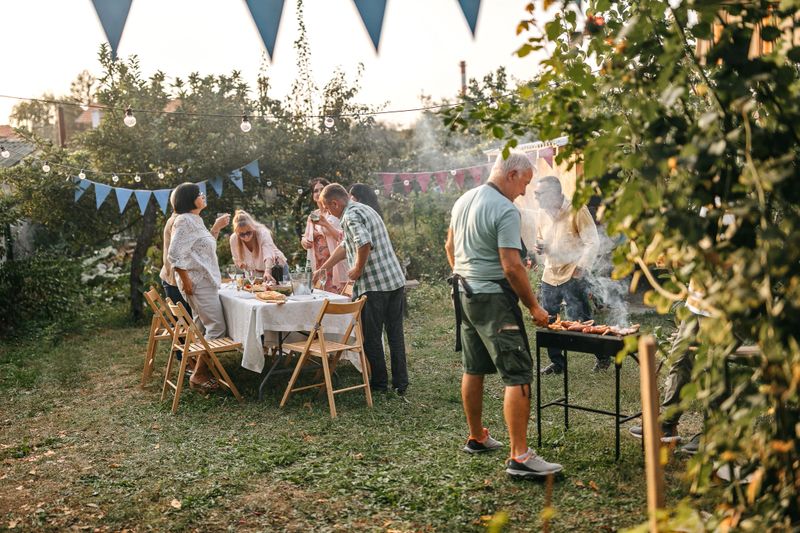 Senior man making barbeque for his friends during open garden party