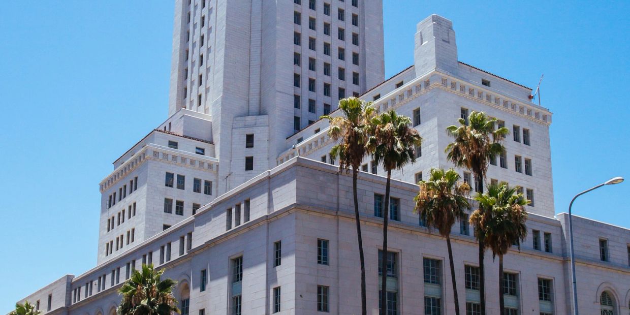 Tall white marble building with palm trees under bright blue sky.