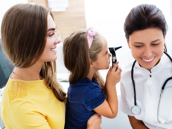 Child having ear examination by a smiling female doctor while mother watches.