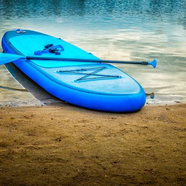 Blue paddleboard resting on sandy shore by water.