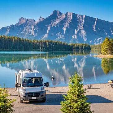 A camper van parked near a serene lake with mountains in the background.
