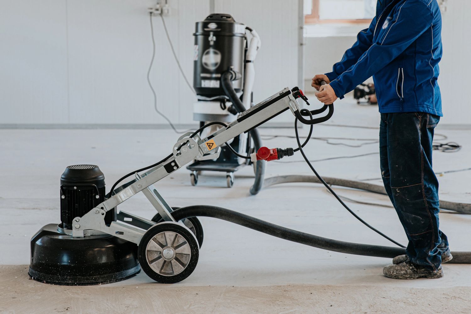 Worker operating a floor polishing machine on a concrete surface indoors.