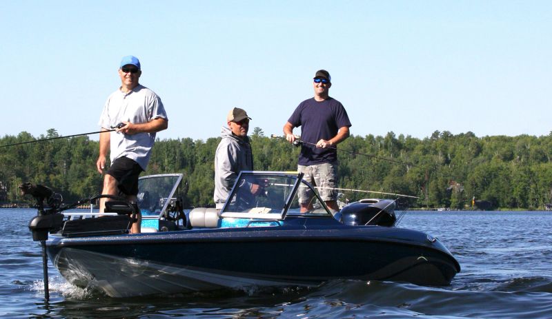 Three middle aged men are enjoying a sunny day out on the water fishing.  The water is a freshwater lake in the western part of the Great Lakes region of the United States.