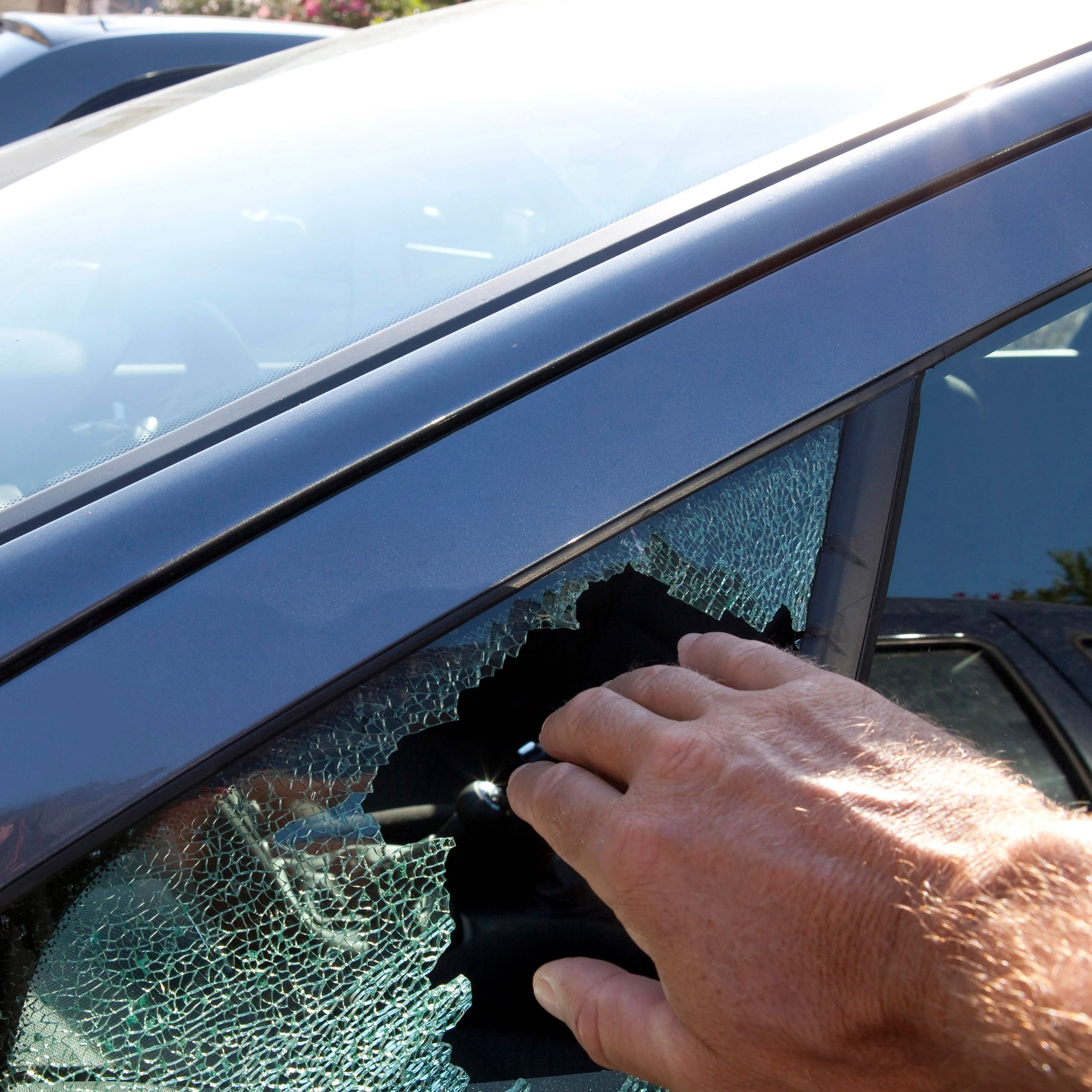 A hand reaching through a shattered car window.