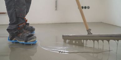 Worker leveling wet concrete floor wearing spiked shoes.
