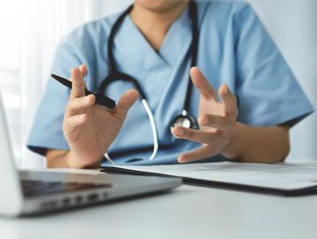 Doctor explaining with hands while sitting at desk.
