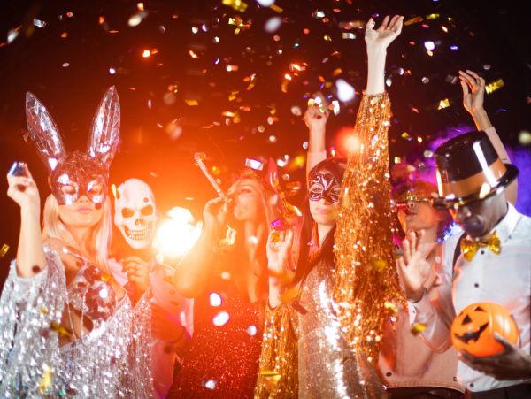 People in festive costumes celebrating with confetti and masks at a party.