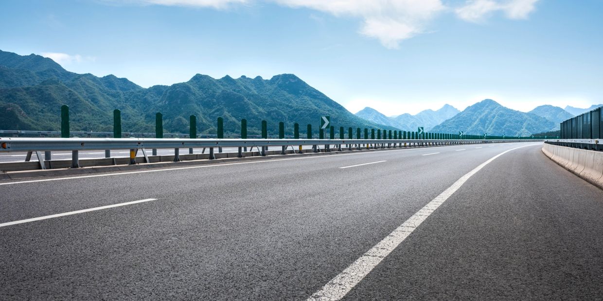 Empty highway winding through mountainous terrain under a clear sky.