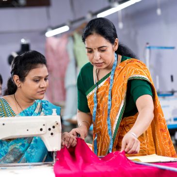 Two women working on fabric with a sewing machine.