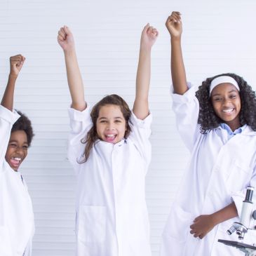 Three happy young girls in lab coats celebrating.