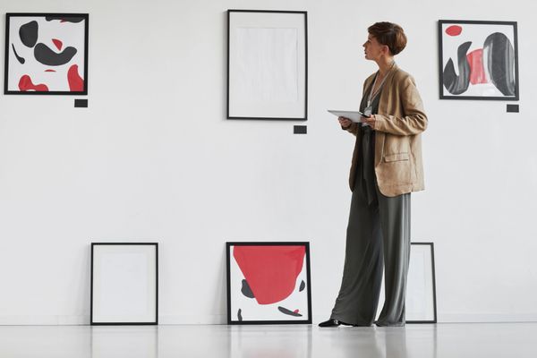 A woman observes abstract art in a gallery, holding a tablet.