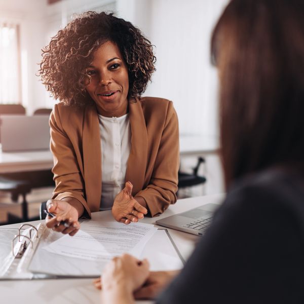 A professional woman discussing documents with a colleague in an office setting.