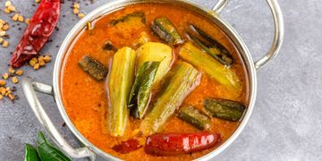 A pot of spicy Indian drumstick sambar with curry leaves and dried red chili.