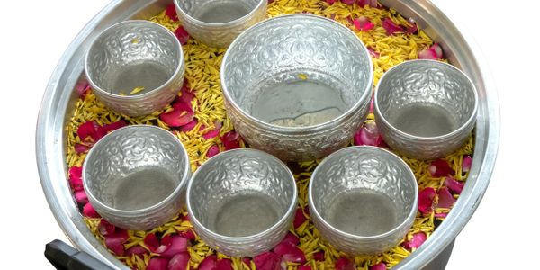 Decorative silver bowls arranged on a bed of yellow rice and rose petals.