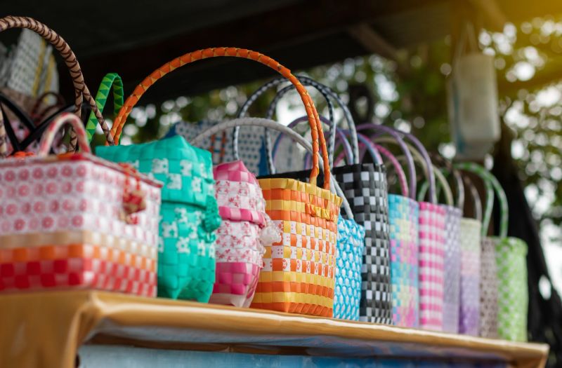 A group of woven plastic baskets, colorful and beautiful, which are handicrafts placed on the table for retail sale in rural stores commonly seen in Thailand.