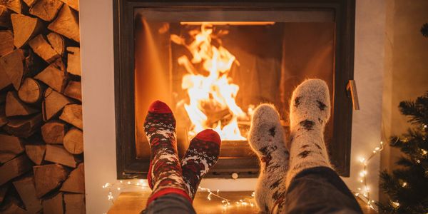 Two people warming their feet by a cozy fireplace wearing festive socks.
