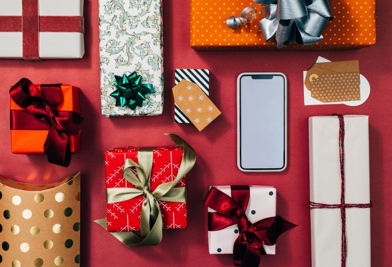 Beautifully wrapped Christmas presents of various shapes and sizes and a mobile phone in a flat lay still life.
