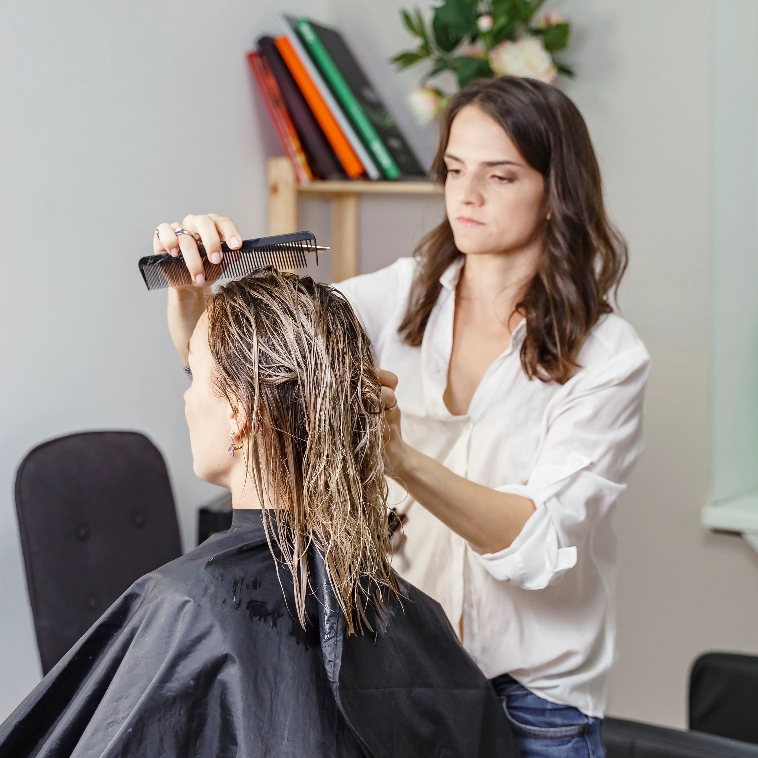 A hairstylist carefully combs wet hair of a client in a salon.