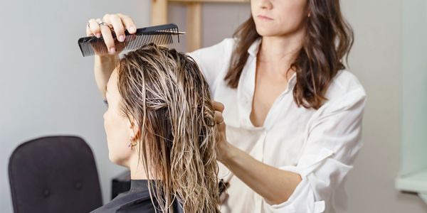 A hairdresser combing wet hair of a seated client.