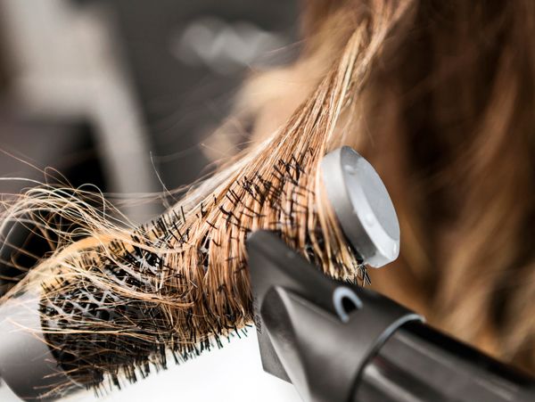 Close-up of hair being styled with a round brush and hair dryer.