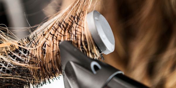 Close-up of hair being styled with a round brush and hair dryer.