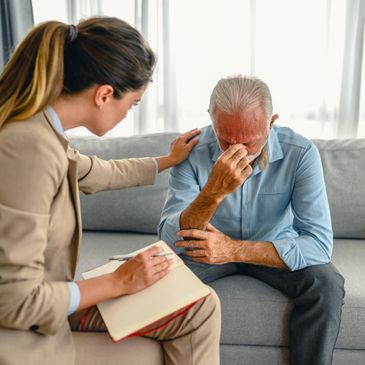 A woman comforts a distressed elderly man during a therapy session.