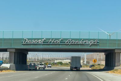 Highway underpass sign reads Desert Hot Springs with wind turbines in the background.