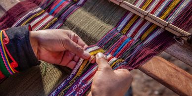 Manos tejiendo una tela colorida tradicional.