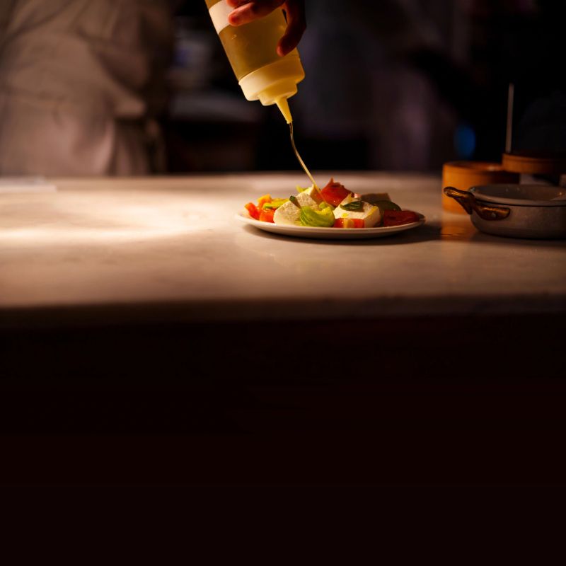Adding olive oil to a caprese salad
