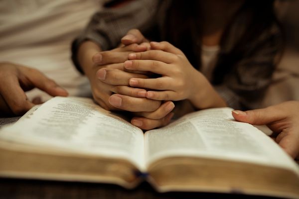 Two people holding hands over an open book, symbolizing support and connection.