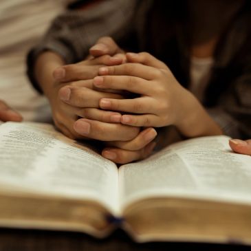 Hands clasped together over an open book.