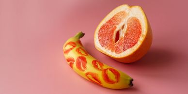 Banana with lipstick prints and a grapefruit half on a pink background.
