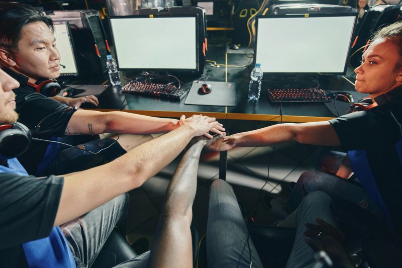 Online video games competition. Professional multiracial cyber sport team putting hands together before starting eSports tournament