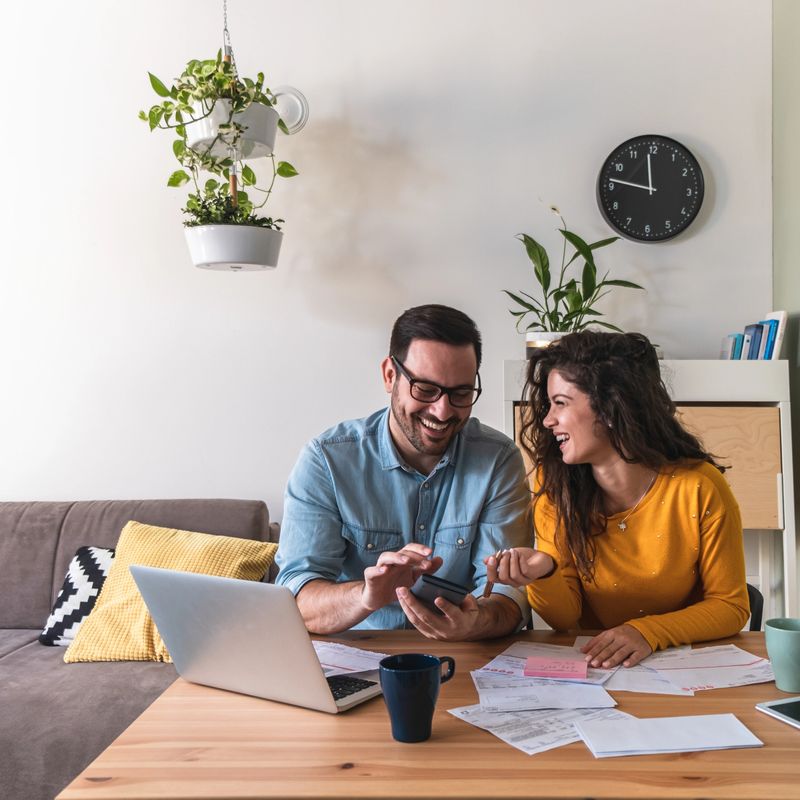Happy husband and wife paying bills online on laptop computer at home