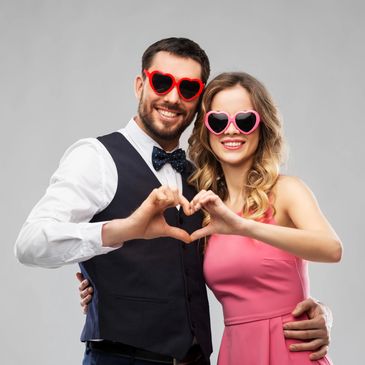 Happy couple wearing heart-shaped sunglasses making a heart gesture.