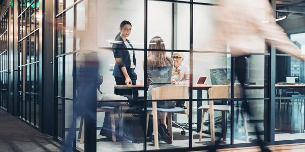 Business meeting in a glass office with people moving outside.