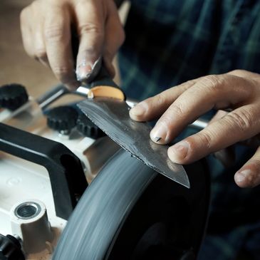 Close-up of hands sharpening a knife on a grinding wheel.