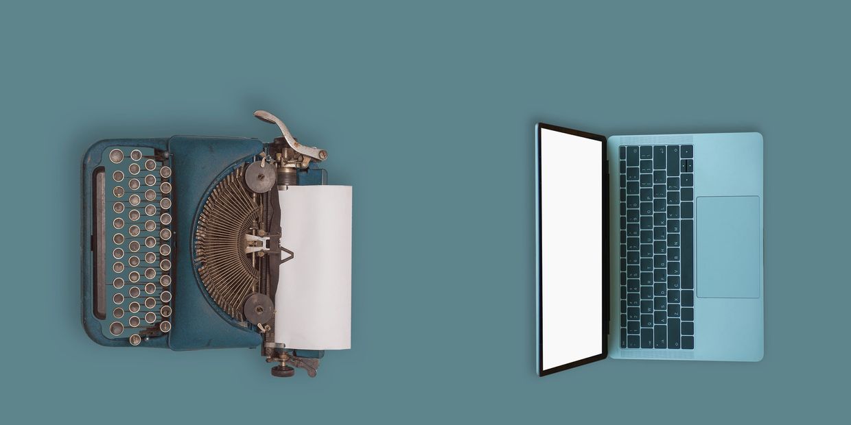 Vintage typewriter and modern laptop side by side on blue background.
