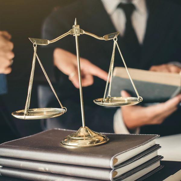 Scales of justice on law books with professionals in background.
