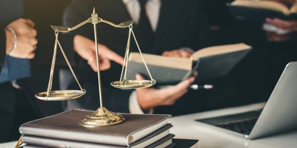 Scales of justice on law books with professionals in background.