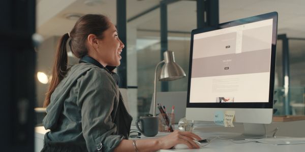 Woman happily working on a desktop computer in a modern office.