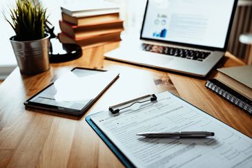 Workspace with tax form, pen, tablet, laptop, books, and plant on wooden desk.