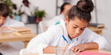 A focused student writing at a desk in a classroom.
