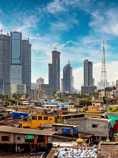 Contrasting cityscape with colorful slums in front and towering skyscrapers behind under a blue sky.