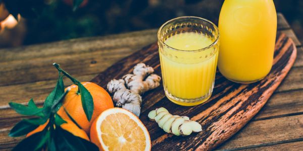 Glass and bottle of orange juice with fresh oranges and ginger on wooden board.