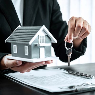Person holding a house model and keys above a contract on a desk.