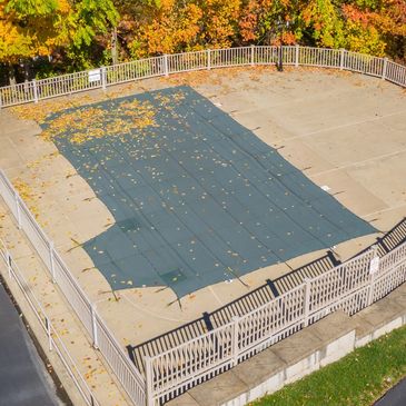 Covered outdoor pool surrounded by autumn foliage and a small building.