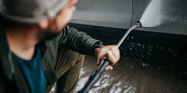Person washing a car using a high-pressure water hose.