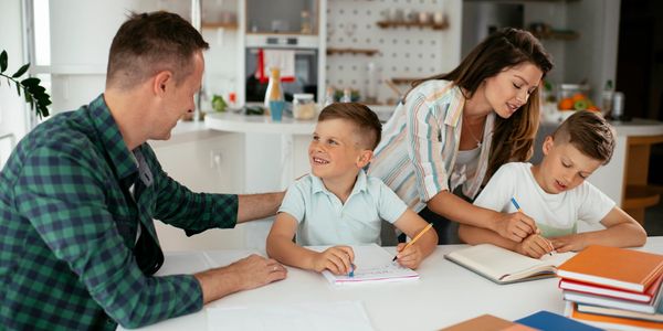 Parents helping their children with homework at a kitchen table.